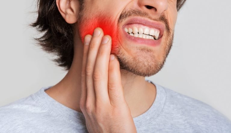 A man holding his jaw with his hand and grimacing, there is a red highlighted area on his jaw highlighting where the pain is.