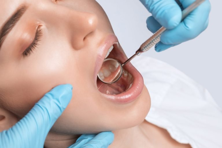 A young woman with a dentist wearing gloves inspecting her mouth with a dental mirror.