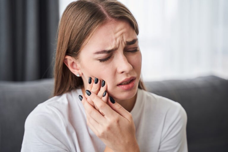 A woman holding her hands to the right side of their jaw. wincing as they experience pain from a root canal